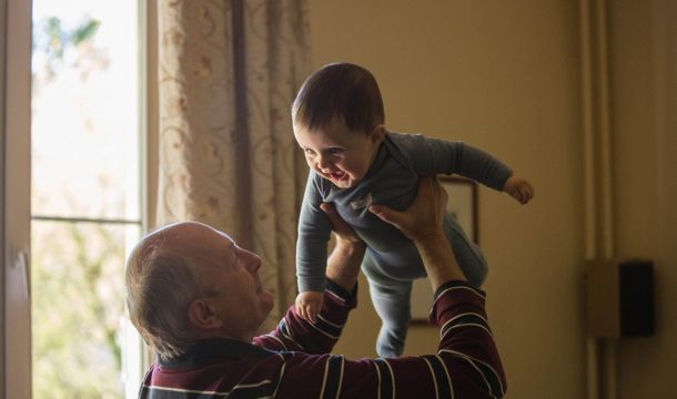 grandfather playing with young child indoors, by window